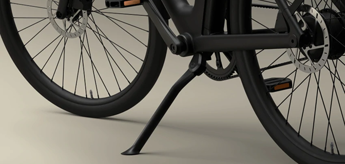 Lower part of the electric bike showing the black wheel rim, disc brake, and a sturdy kickstand.